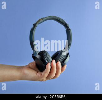 Cuffie wireless nere in mano su sfondo blu Foto Stock