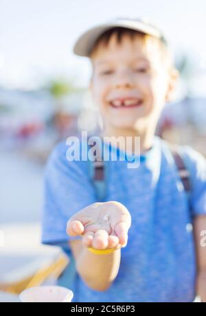 Felice ragazzo giovane che mostra un dente che ha appena perso. Il dente in una mano a fuoco. Foto Stock