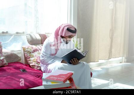 Uomo arabo Saudita seduto su divano/divano in soggiorno e lettura libri Foto Stock