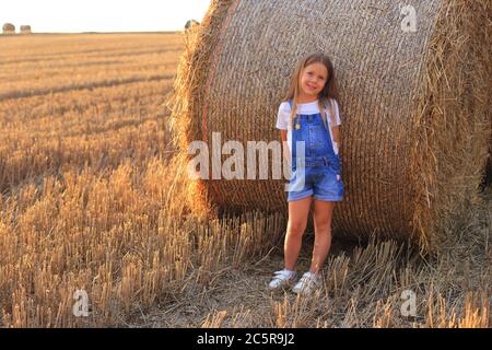 Bella bambina si trova vicino ad un fienino in un campo estivo Foto Stock