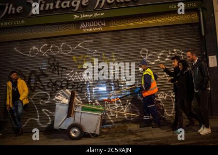 Un pulitore di strada passa in una strada a Soho, mentre i bevitori di tarda notte continuano nelle prime ore della domenica mattina, mentre le restrizioni di blocco del coronavirus sono attenuate in tutta l'Inghilterra. Foto Stock