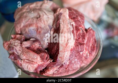 Recipiente grande in vetro con pezzi di carne rossa arrosto di manzo intero con fondo sfocato e ingredienti di consistenza cucinati Foto Stock