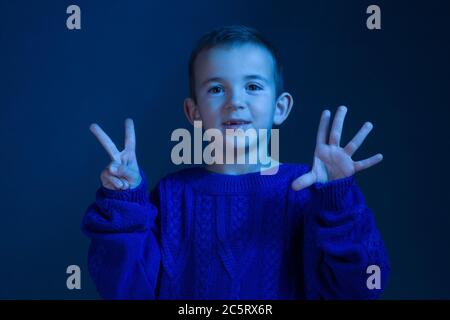 Ritratto in studio di una brunetta Boy che conta sulle dita, mostra sette dita, tonificanti in un classico colore blu. Foto Stock