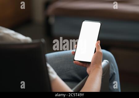 Giovane donna seduta in sedia con smartphone moderno con bianco schermo Foto Stock