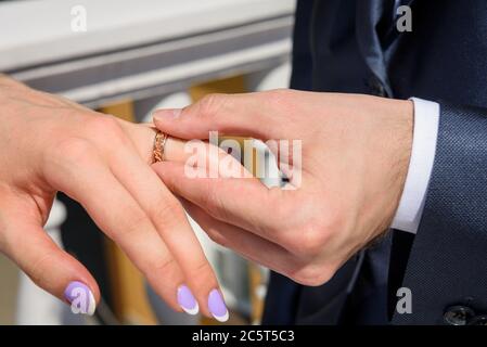 Sposo e sposo si mettono gli anelli d'oro l'uno sull'altro su un dito e li mostrano sulle loro mani. Foto Stock