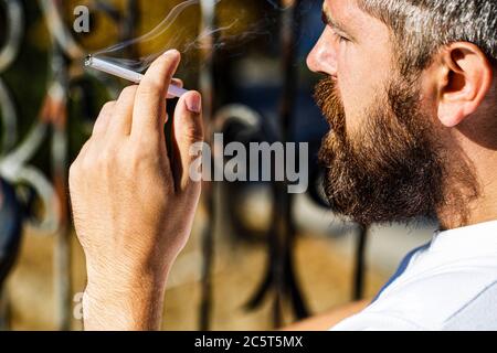 Uomo bearded con sigaro. La barba e i baffi fumano il sigaro. Sigari che smolderano. Fumatore maschio, sigaro fumatore. Uomo che fuma con barba. Giovane uomo hipster Foto Stock