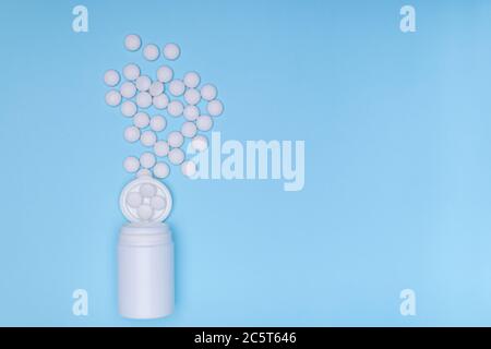 Vasetto di medicina bianca e pillole bianche sparse su sfondo blu pastello. Medicinale e prescrizione pillole bianche sfondo piano.Copia spazio Foto Stock