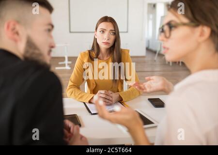 Giovane donna in blusa che guarda attentamente i datori di lavoro mentre passa il tempo in ufficio moderno. Donna richiedente in attesa dei risultati del colloquio di lavoro Foto Stock