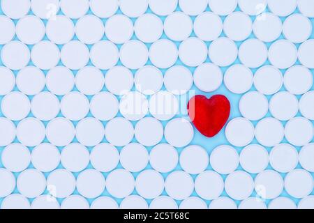 Concetto di assistenza sanitaria globale. Piccolo cuore rosso. Sfondo di pillole bianche macro con un cuore rosso sdraiato su uno sfondo blu, vista dall'alto. Foto Stock