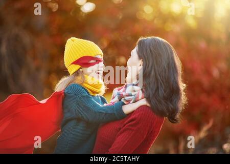 Buona famiglia sulla passeggiata autunnale! Madre e figlia camminano nel Parco e godono della splendida natura autunnale. La bambina gioca supereroe. Foto Stock