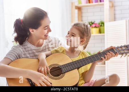 Buona famiglia. Madre e figlia suonano insieme la chitarra. Donna adulta che suona la chitarra per bambina. Foto Stock