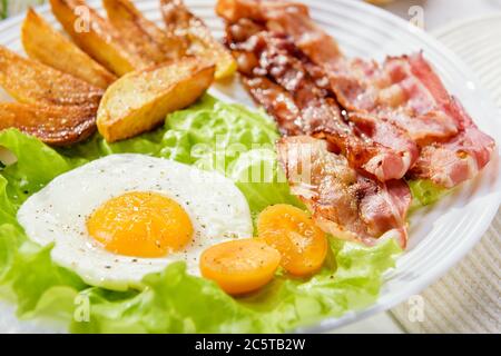 Pancetta fritta con patatine fritte e un uovo delicato, primo piano. Foto Stock