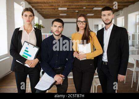 Gruppo di persone aziendali serie in tute che guardano con attenzione in macchina fotografica insieme mentre si passa il tempo al lavoro in un ufficio moderno Foto Stock