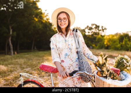 Sorridente ragazza in occhiali in bicicletta con cesto pieno di frutta Foto Stock