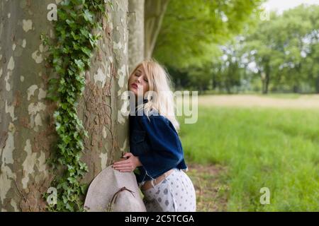 Giovane e bella donna bionda abbracciando un enorme vecchio albero Foto Stock