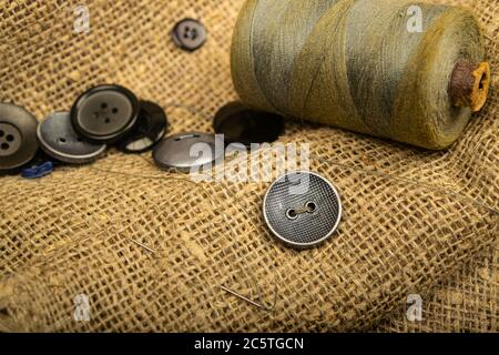 Bottoni diversi e una bobina di filo sulla tela con una texture ruvida. Primo piano Foto Stock