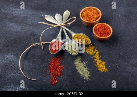 Vista dall'alto di diversi tipi di spezie colorate in cucchiai su una superficie di pietra nera. Struttura creativa del concetto di cibo con spazio vuoto per la copia del messaggio Foto Stock