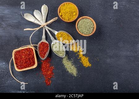 Vista dall'alto di diversi tipi di spezie colorate in cucchiai su una superficie di pietra nera. Struttura creativa del concetto di cibo con spazio vuoto per la copia del messaggio Foto Stock