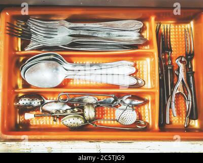 Foto di un contenitore di plastica arancione con cucchiai, forcelle e coltelli vecchi Foto Stock