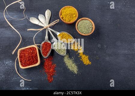 Vista dall'alto di diversi tipi di spezie colorate in cucchiai su una superficie di pietra nera. Struttura creativa del concetto di cibo con spazio vuoto per la copia del messaggio Foto Stock