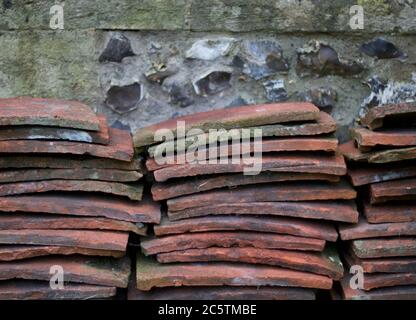 Pile di vecchie tegole in terracotta accatastate contro pareti di pietra focaia stagionato Foto Stock