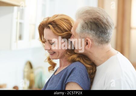 Vista laterale ritratto di coppia matura amorevole con l'uomo che sussurra a sorridente elegante donna, copia spazio Foto Stock