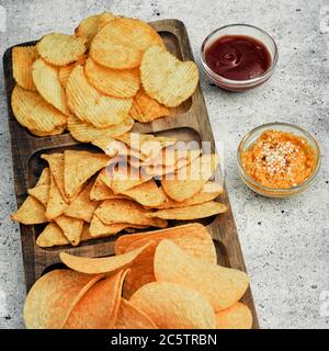 Patatine, spuntini e cracker su un asse di legno. Fast food. Foto Stock