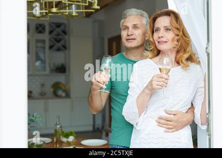 Vita in su ritratto di coppia matura elegante godendo di champagne mentre si guarda fuori dalla finestra alla terrazza, spazio copia Foto Stock