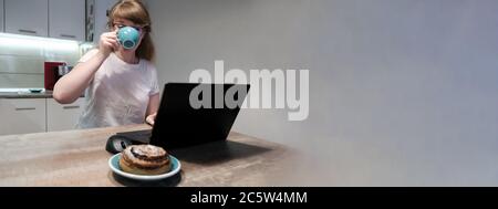 Giovane donna che beve il caffè del mattino con il computer portatile, godendo di lavoro remoto a casa. Spazio di copia Foto Stock