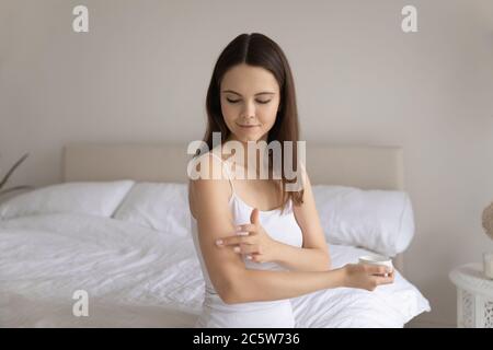 Bella giovane donna soddisfatta che applica crema idratante sul braccio Foto Stock