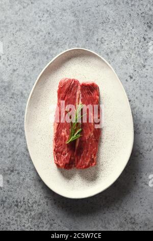 Bistecca di ribeye cruda con rosmarino su grigio. Foto Stock