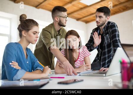 Gruppo di uomini e donne d'affari che lavorano con cura con schizzi mentre trascorrono il tempo al lavoro. I giovani discutono emotivamente di un nuovo progetto Foto Stock