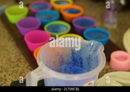 Fondere il sapone in una tazza di plastica e aggiungere colori e profumi prima di versare in stampi di silicone colorati per far fondere e versare il sapone fatto in casa Foto Stock