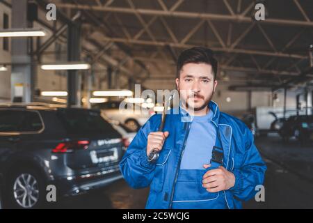 Ritratto di un meccanico di automobile che tiene la chiave sulla sua spalla. Meccanico automatico in garage Foto Stock