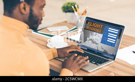 Uomo d'affari africano al volo di prenotazione del laptop seduto in ufficio, Panorama Foto Stock