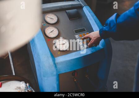 Il meccanico automatico preme un pulsante sulla macchina per rifornire i condizionatori d'aria della vettura Foto Stock