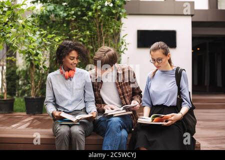 Gruppo di studenti seduti su panchina e leggendo libri nel cortile dell'università Foto Stock
