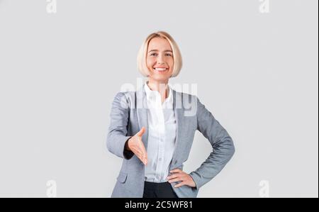 Felice donna d'affari matura che estende la sua mano per scuotere su sfondo chiaro Foto Stock