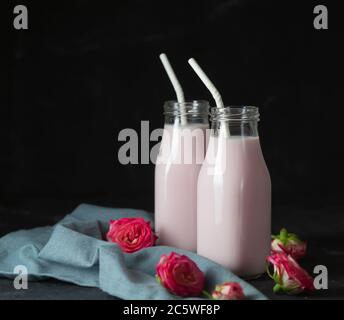 Il latte lunare si prepara con il fiore rosa in due bottiglie su sfondo nero. Drink rilassante alla moda a base di tradizioni ayurvediche Foto Stock