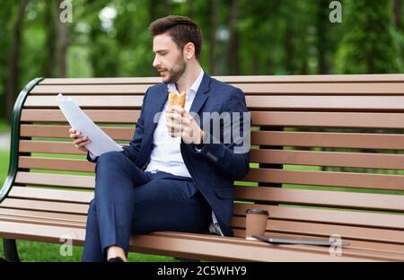 CEO che lavora duramente per esaminare i documenti mentre si pranza sul banco di lavoro al parco Foto Stock