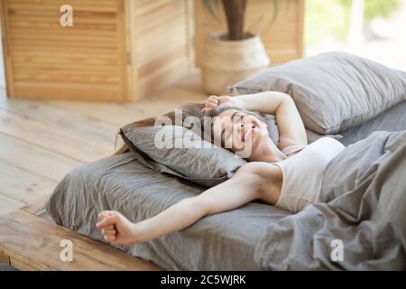 Giovane donna assonnata svegliandosi nel letto e stirandosi al sole Foto Stock