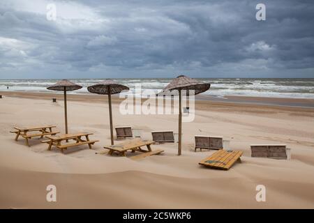 Egmont aan Zee, Paesi Bassi - Giugno 29,2020: Il ristorante vuoto sulla spiaggia. I tavoli coperti di sabbia sulla spiaggia. La spiaggia senza turisti stranieri Foto Stock