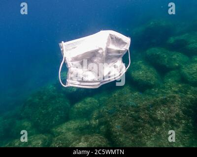 La gente getta fuori una maschera medica sul mare. Maschere chirurgiche usate galleggianti sott'acqua del mare. Maschera igienica inutile del coronavirus. Informazioni Foto Stock