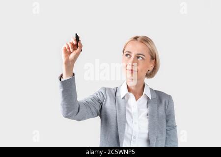 Attraente donna di affari che scrive o che disegna sullo schermo virtuale contro sfondo chiaro, spazio per il disegno Foto Stock