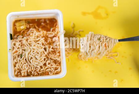 Primo piano di tagliatelle pronte all'uso con spezie su sfondo giallo. Forchetta con macaroni avvitanti vicino al piatto. Foto Stock