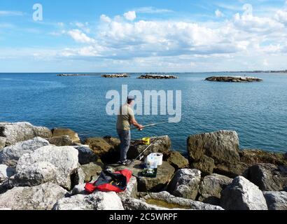 Pescatore sulle rocce di Cesenatico. Mare Adriatico. Italia Foto Stock