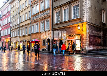 Varsavia, Polonia - 22 dicembre 2019: Turisti che camminano con ombrelloni shopping nel centro storico di Warszawa in serata pioggia durante la riflessione invernale su p. Foto Stock