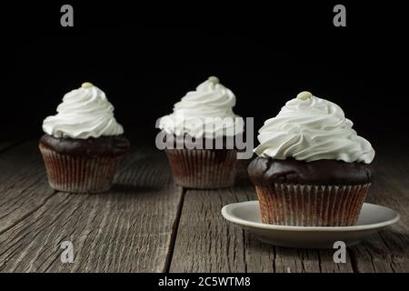 Cupcake fatto in casa in carta patty case è in piedi su un piccolo piatto di ceramica; due più cupcakes sono in uno sfondo sfocato. Foto Stock