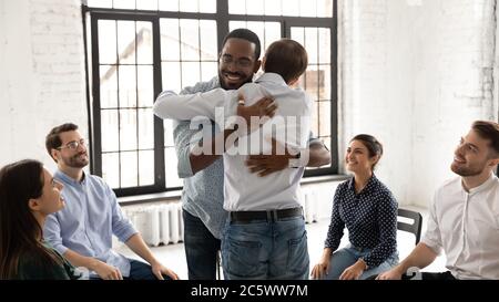Uomini africani e caucasici che abbracciano durante la sessione di consulenza di terapia di gruppo Foto Stock
