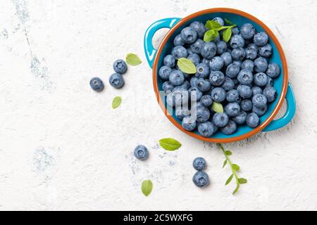 Mirtilli freschi maturi con foglie in un recipiente su un tavolo di pietra, vista dall'alto con spazio per la copia Foto Stock